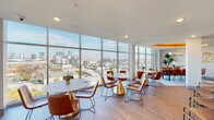 This sophisticated amenity floor is thoughtfully designed to offer a range of social and recreational spaces, all unified by a cohesive mid-century modern aesthetic. Wide-plank hardwood flooring flows throughout the main areas, complemented by warm wood accents, rich cognac leather furnishings, and curated contemporary artwork adorning the walls.

The expansive lounge serves as the heart of the floor, featuring plush leather sofas and armchairs arranged around a built-in wood entertainment wall with a fireplace and large-screen TV. An artistic chandelier adds a warm focal point to the seating area. Adjacent to the lounge, a dedicated game room with warm amber-toned walls houses a striking hardwood pool table beneath a modern globe pendant light.

A fully equipped wet bar with granite countertops, wood cabinetry, a deep sink, and under-counter beverage coolers provides convenient refreshment service for gatherings. The dining and lounge areas along the building's perimeter are bathed in natural light from floor-to-ceiling glass curtain walls, offering sweeping panoramic views of the surrounding urban skyline. A dramatic oval gold-leaf ceiling medallion crowns the formal dining area, where a large communal table with leather seating sits beneath a statement pendant light. Lush potted tropical plants add a vibrant, natural touch throughout the space.