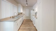 This single-floor residence offers a clean, functional layout with a bright and open living area at its heart. The living space features light wood-look flooring, neutral gray-toned walls, and a textured ceiling, with a wall-mounted air conditioning unit and sliding glass doors fitted with vertical blinds that invite natural light and provide access to an outdoor area. The galley-style kitchen is efficiently designed with white cabinetry lining both sides, gray countertops, a stainless steel double sink, and white appliances including a refrigerator, electric range, microwave, and dishwasher. Track lighting overhead adds a practical, modern touch. A second living or flex area continues the wood-look flooring and features a ceiling fan, offering versatile usage options. The bedrooms are carpeted in a soft gray tone, providing a comfortable and quiet retreat. One bedroom benefits from a window with natural views, while another includes a mirrored sliding closet door. The bathroom is straightforward and well-maintained, featuring wood-look flooring, a shower-tub combination, toilet, and a vanity with a stone-look countertop. Throughout the space, consistent neutral tones and clean finishes create a cohesive and move-in-ready atmosphere.