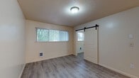Located at 16124 SE Alder St in Portland, Oregon, this single-floor unit offers a practical and comfortable layout with consistent vinyl plank flooring flowing throughout. The kitchen is well-equipped with warm wood cabinetry, granite-look countertops, a stainless steel sink, a dishwasher, an electric range with overhead ventilation, and a refrigerator. Tiled walls provide a clean, functional backdrop behind the cooking area. The open living and dining areas extend from the kitchen, benefiting from natural light streaming through windows that frame views of surrounding greenery. A standout feature is the stylish sliding barn door that connects living spaces, adding a modern, space-saving design element. The living area also includes a wall-mounted electrical panel and individual room heating units. The bathroom is clean and straightforward, featuring a full tub-shower combo with classic white tile surround, a single vanity with sink, and light wood-tone flooring. Textured ceilings are present throughout the unit. The layout is efficient and open, making great use of the available space. With its lush outdoor views, functional kitchen, and updated flooring, this unit offers a comfortable living environment in a convenient Portland location.