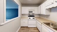 Located at 524 Bramlet Rd in Charlotte's 28205 zip code, this single-floor, one-bedroom, one-bathroom residence offers a well-organized layout across a compact but functional footprint. The combined living and kitchen area serves as the heart of the home, highlighted by durable wood-look flooring and a striking painted blue-gray brick accent wall that adds character and visual depth. A pass-through window connects the living area to the kitchen, creating an open feel while maintaining distinct zones. The kitchen is outfitted with white cabinetry, light countertops, a full suite of white appliances including a range, over-the-range microwave, and dishwasher, and continues the wood-look flooring for a cohesive look. A hallway connects the main living space to the private areas of the home. The bedroom features soft wall-to-wall carpeting, neutral gray walls, and a window that allows natural light to filter in. The bathroom is clean and classic, featuring a white tiled tub-shower combination with chrome fixtures. Throughout the space, white baseboards and trim provide a crisp, finished contrast to the neutral gray walls, lending the home a tidy, move-in-ready appearance.