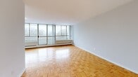 Located at 35-49 Thorncliffe Park Dr in Toronto's Thorncliffe Park neighbourhood, this well-appointed one-bedroom, one-bathroom unit offers a generous and functional layout across a single floor. The living room is a standout feature, bathed in natural light through expansive floor-to-ceiling windows that frame serene treetop views. Classic parquet wood flooring runs throughout the living and bedroom areas, adding warmth and character to the clean, neutral palette of light grey walls and white trim. The separate kitchen is efficiently designed with white cabinetry, a double sink, laminate countertops, tile flooring, and white appliances including a refrigerator and electric range. A convenient doorway connects the kitchen directly to the bright living area. The spacious primary bedroom offers ample room and direct access to a large walk-in closet fitted with dual hanging rods — ideal for organized storage. The bathroom is finished in a clean, minimalist style with white walls, tile flooring, a vanity with mirror, and a full-width towel bar. A hallway connects all rooms cohesively, completing this practical and comfortable urban residence.