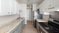 This single-story residence presents a clean, updated interior with a cohesive neutral color palette throughout. The kitchen serves as a functional centerpiece, featuring a galley-style layout with two-tone cabinetry — white upper cabinets paired with sage-green lower cabinets — complemented by granite-look countertops and stainless steel appliances, including a refrigerator and electric range. A window allows natural light to brighten the space.

Adjacent to the kitchen, the dining area offers an open, airy feel with light wood-look flooring that extends consistently throughout the unit. The living area is generously proportioned, with neutral taupe walls and white trim providing a versatile backdrop.

The bedrooms are well-sized, with one room featuring dual windows that bring in ample natural light. Both rooms offer light flooring and closet access, creating practical, comfortable spaces.

The bathroom includes a white vanity with an integrated sink, a large wall mirror, and easy access to the central hallway. The hallway connects all rooms efficiently, as illustrated by the 3D layout view, which reveals a straightforward, well-organized floor plan designed for comfortable everyday living.