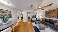 This two-story home is thoughtfully laid out across two floors, offering two bedrooms, two bathrooms, an office, and a combined living, dining, and kitchen area. The main floor features warm hardwood-style flooring throughout, crown molding, and textured ceilings. The open living room is anchored by a ceiling fan and built-in shelving, creating a functional and inviting gathering space. Adjacent to the living area, the galley-style kitchen is equipped with rich dark wood cabinetry, granite-style countertops, and stainless steel appliances. The dining area benefits from a window that brings in natural light. A full bathroom on the main floor includes a wood-framed vanity mirror and granite countertop. Upstairs, the primary bedroom offers sliding glass doors that open to a private balcony with outdoor views, complemented by a ceiling fan and carpet flooring. The second bedroom doubles as a versatile office space, featuring its own closet, a window, ceiling fan, and carpet. A dedicated closet provides additional storage. Both floors are connected by a staircase, and the overall layout offers a practical, well-organized flow suitable for everyday living.