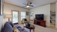 Located at 12105 SH-151 W in San Antonio, Texas, this single-floor residence offers a thoughtfully designed layout with comfortable living spaces and quality finishes throughout. The living room serves as the heart of the home, featuring plush carpeting, crown molding, a ceiling fan, and built-in shelving flanking a central media area. Natural light filters in through multiple windows with blinds, and a glass door opens to a private balcony, bringing the outdoors in. The space flows seamlessly toward a dedicated dining nook, where there is room for intimate gatherings around a round table. The kitchen is outfitted with warm wood cabinetry, granite countertops, hardwood-style flooring, and full-size appliances, connecting conveniently to the rest of the home via a practical hallway. The bedroom is a serene retreat, offering carpeted floors, multiple windows dressed with elegant draping curtains, and ample room for full bedroom furniture. The bathroom features rich dark wood vanity cabinetry topped with granite countertops, a generous mirror, and hardwood-style flooring, providing a clean and polished aesthetic. Throughout the residence, a neutral color palette, consistent trim work, and ceiling fans contribute to a cohesive and inviting ambiance.