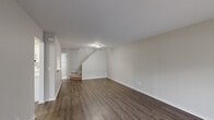 This two-story home offers a clean, functional layout with thoughtful finishes throughout. The main level features a spacious living area with rich, dark hardwood-style flooring, neutral walls, and a staircase leading to the upper floor. A sliding glass door floods the living space with natural light and provides views of the lush greenery outside. The kitchen is outfitted with crisp white shaker-style cabinetry, black hardware accents, white countertops, and matching white appliances, all set over warm wood-look flooring. A dedicated utility area on the main level houses a washer, water heater, and furnace, providing convenient in-unit mechanicals. Upstairs, the bedrooms are finished with plush wall-to-wall carpeting and neutral tones. The primary bedroom is a standout, featuring a distinctive arched window that frames outdoor tree views and adds architectural character. Additional bedrooms offer hardwood-style flooring and standard windows with garden views. Throughout the home, clean white trim, flush-mount lighting, and a consistent neutral palette create a cohesive and welcoming atmosphere well-suited for comfortable everyday living.