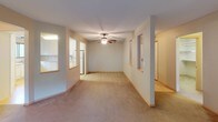 Located at 3185 Karth Rd in White Bear Lake, Minnesota, this single-floor residence offers a thoughtfully laid-out living space with a neutral, warm color palette throughout. The open living and dining area is carpeted and anchored by a ceiling fan, with pass-through openings connecting to the kitchen, creating an open and connected feel. Sliding glass doors lead to a private outdoor balcony, filling the space with natural light and offering views of surrounding greenery. The kitchen features white cabinetry, light countertops, and white appliances including an electric range with overhead microwave, all set above light hardwood-style flooring. The bedrooms are carpeted and each include windows with vertical blinds overlooking wooded outdoor views, individual climate control units, and baseboard heating. Two bathrooms serve the residence: one with a tiled shower-tub combination and a vanity with granite-style countertops, and a second with a corner stand-up shower enclosed in frosted glass doors. Both bathrooms are finished with coordinating countertops and mirrors. The overall ambiance is clean, functional, and well-maintained, making this a practical and comfortable single-level home.