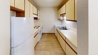 This efficiently designed single-floor unit offers a practical and comfortable layout across four distinct spaces: a living area, bedroom, kitchen, and bathroom. The open living area is finished with neutral-toned carpet and features a wall-mounted air conditioning unit, a baseboard heating system, and vertical blinds over a sliding glass door that provides access to the outdoors and brings in natural light. A ceiling fan is visible from the living space, serving the adjacent bedroom.

The bedroom is a well-proportioned, carpeted room equipped with its own ceiling fan and light fixture, a baseboard heater beneath a window with vertical blinds, and a generously sized closet with bi-fold doors and built-in shelving for organized storage.

The galley-style kitchen is lined on both sides with cream-toned cabinetry featuring warm wood trim, offering ample upper and lower storage. White appliances including a refrigerator, electric range, and a dishwasher are neatly integrated, while light wood-look flooring and a stainless steel sink complete the functional space.

The bathroom includes a tub-shower combination fitted with grab bars and a handheld showerhead, a toilet, and a vanity with a dark-toned cabinet base. Tile-look flooring and a textured ceiling tie the room together. A hallway connects all rooms, providing a logical and efficient flow throughout the unit.