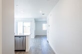 This well-designed two-story home showcases a clean, contemporary aesthetic with light-toned wood-look flooring and crisp white walls throughout. The heart of the home is a modern kitchen equipped with stainless steel appliances, including a refrigerator, range, and over-the-range microwave. Shaker-style white cabinetry provides ample storage, while a large kitchen island with a built-in sink and white quartz countertops offers generous workspace and a natural gathering spot. Recessed lighting illuminates the space efficiently. The open layout connects the kitchen seamlessly to the adjacent living area, which benefits from sliding glass door access and multiple windows that invite natural light and outdoor views. The bedrooms are bright and spacious, featuring large windows with blinds and light wood-look flooring. A full bathroom includes a tub-shower combination with tiled surround, a white vanity, and wood-look flooring. A convenient half bath on the main level features a pedestal sink and oval mirror. The dedicated laundry room houses a full-size washer and dryer alongside overhead shelving and a bright window. The two-floor layout provides practical separation between living and private spaces, making this home functional and inviting throughout.