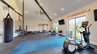 Located at 625 US-29 in Athens, Georgia, this single-floor fitness facility is designed to support a wide range of training disciplines in a bright, well-appointed environment. The entry foyer greets visitors with soaring vaulted ceilings, warm hardwood flooring, large glass double doors, and motivational branded signage, setting an energetic tone from the moment you arrive. A built-in mudroom area with hooks, cubbies, and floor-to-ceiling windows provides a functional and light-filled transition into the workout spaces.

The main gym area is the centerpiece of the facility, featuring dramatic cathedral ceilings with exposed wood beam accents and oversized industrial ceiling fans for airflow. Rubber tile flooring covers the expansive workout floor, which is outfitted with a full dumbbell rack, medicine balls, a power rack, benches, a rowing machine, an elliptical, a stationary bike, a treadmill, and a central pull-up/suspension rig with a hanging heavy bag. Large windows and sliding glass doors flood the space with natural light and offer views of the surrounding greenery.

A separate studio room features hardwood floors, a wall-length mirror, a mounted ballet barre, and large windows, making it ideal for yoga, stretching, or barre classes. Inspirational quotes adorn the walls throughout, reinforcing the facility's motivating atmosphere.