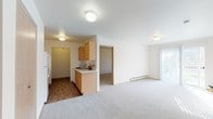This single-floor residential unit offers a clean, functional layout designed for comfortable everyday living. The open living and dining area is finished with plush wall-to-wall carpeting and bright white walls, creating a light and airy atmosphere. A sliding glass door floods the space with natural light and provides views of surrounding greenery, while a baseboard heating system ensures year-round comfort. The galley-style kitchen is efficiently designed, featuring warm honey-toned wood cabinetry, white countertops, a double sink, and white appliances including a range and refrigerator. Rich wood-look flooring runs throughout the kitchen, adding warmth and contrast to the neutral palette. Two carpeted bedrooms offer generous space, with natural light streaming in through large windows framing pleasant outdoor views. One bedroom includes a reach-in closet with a hanging rod, while the other connects conveniently to the bathroom. The full bathroom is well-appointed with a wood-toned vanity, a wide countertop with an integrated sink, a large mirror, and a shower-tub combination, all set on wood-look flooring. Throughout the unit, warm wood-toned door and trim details tie the interior together with a cohesive, welcoming aesthetic.