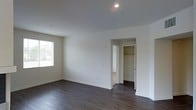 This single-floor space presents a clean, modern aesthetic defined by a neutral color palette and thoughtfully chosen finishes throughout. The interior features rich, dark hardwood flooring that contrasts beautifully against the crisp white walls and ceilings, lending a sense of warmth and sophistication to the space. Recessed lighting is installed throughout, providing even, ambient illumination that complements the natural light that filters in through a window, brightening the room and enhancing its open feel. The walls are finished smoothly with classic white baseboards that frame the floors with a polished look. A standout feature is the walk-in closet, accessible through a dedicated doorway and equipped with built-in shelving and a hanging rod, offering practical and organized storage. The overall layout is straightforward and functional, with an open room configuration that provides flexibility for various uses. The minimalist design and quality finishes come together to create a bright, airy ambiance that is both welcoming and versatile. The space is well-suited for those seeking a modern, low-maintenance environment with clean lines and durable materials.