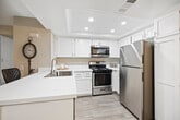 Located at 1265 E 9th St in Upland, California, this single-floor residence offers a clean, modern interior defined by consistent light wood-look flooring and a neutral warm-gray color palette throughout. The thoughtfully laid-out floor plan connects a series of well-proportioned rooms, each benefiting from natural light streaming through large windows dressed with vertical blinds. Several rooms feature sliding closet doors, providing ample built-in storage. One room opens directly to an outdoor patio area via sliding glass doors, offering a seamless indoor-outdoor connection. The updated kitchen is a standout feature, showcasing white shaker-style cabinetry, a crisp white countertop, recessed lighting, and a full suite of stainless steel appliances including a gas range, over-the-range microwave, dishwasher, and refrigerator. A hallway connects the living areas to the bathroom, which includes white shaker-style cabinetry with brushed hardware, a white countertop vanity, and wood-look tile flooring that ties cohesively to the rest of the home. A central hallway with multiple closet doors provides additional storage solutions. The overall ambiance is bright, clean, and move-in ready, reflecting a fresh and contemporary aesthetic throughout.