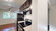 This single-floor, one-bedroom, one-bathroom unit is thoughtfully laid out to maximize its compact footprint. The combined kitchen and living area forms the heart of the space, where rich hardwood-style flooring runs throughout. The galley-style kitchen is a standout feature, equipped with dark espresso cabinetry offering generous upper and lower storage, stainless steel appliances including a refrigerator, electric range with overhead ventilation, and dishwasher, complemented by light countertops and a mosaic tile backsplash. A ceiling fan and a window bring natural light into the kitchen area.

The living room benefits from a sliding glass door fitted with vertical blinds, providing access to outdoor greenery and filling the room with natural light. A hallway connects the main living areas to the private bedroom, which features plush carpeting, a window with leafy outdoor views, and a full-width sliding-door closet for ample storage. The bathroom maintains the cohesive design aesthetic with a dark wood vanity, mosaic tile accent, a large mirror with overhead lighting, and a tub-shower combination with hardwood-style flooring completing the space.