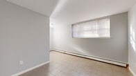 Located at 205 Sigourney St in Hartford, Connecticut, this single-floor unit offers four bedrooms and one bathroom within a efficiently arranged floor plan. The layout connects rooms through a central hallway, providing straightforward access throughout the space.

The bedrooms feature a consistent design with neutral gray walls, parquet-style tile flooring, and baseboard heating units positioned along the walls. Several bedrooms include windows fitted with horizontal blinds, allowing natural light to filter in. At least one bedroom includes a built-in closet with a hanging rod, adding practical storage. The spacious primary bedroom stands out as the largest of the four rooms.

The kitchen is equipped with warm-toned wood cabinetry, a coil-burner electric range, a range hood, and light countertops, providing a functional cooking space. The bathroom features a full soaking tub surrounded by large-format beige tile extending up the walls, along with a privacy window.

A dedicated laundry area is also included within the unit. Throughout, the consistent use of neutral tones, tile flooring, and baseboard heating creates a uniform, practical ambiance suited for efficient everyday living.