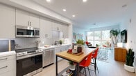 Located in San Diego's vibrant North Park neighborhood, this well-appointed one-bedroom, one-bathroom residence offers a thoughtfully designed single-floor layout. Light wood flooring flows throughout, tying each space together with a cohesive, modern aesthetic.

The kitchen is a standout feature, showcasing gray shaker cabinetry, a herringbone tile backsplash, white quartz countertops, stainless steel appliances, and a matte black faucet. A butcher-block dining table with bold orange chairs adds a lively, contemporary touch and connects seamlessly to the open living area.

The living room is bright and airy, anchored by a large picture window that fills the space with natural light and offers views of the surrounding neighborhood. Clean white walls, recessed lighting, and a warm wood media console create an inviting atmosphere.

The bedroom is a serene retreat, highlighted by a dramatic botanical wall mural, large sliding glass doors with outdoor views, and ample natural light. A dedicated walk-in closet with multi-tier built-in rods and shelving provides excellent storage.

The bathroom features a modern floating vanity with a white undermount sink, backlit mirror, and clean, minimalist finishes. The overall design balances contemporary style with comfortable livability throughout.
