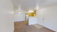 This single-floor, 3-bedroom, 2-bathroom residence offers a well-designed layout that maximizes comfort and functionality. The open-concept living and dining area features neutral wall-to-wall carpeting that creates a warm, inviting atmosphere, while flush-mount and pendant lighting fixtures provide consistent illumination throughout the space. A peninsula-style kitchen is positioned at the heart of the home, featuring warm-toned wood cabinetry, a white refrigerator, and a raised breakfast bar that serves as a natural divider between the kitchen and living areas. The kitchen's tile flooring transitions smoothly from the carpeted living space, adding a practical touch to the cooking area. The layout promotes an easy flow between rooms, making the space ideal for both everyday living and entertaining. The white interior walls and ceilings contribute to a clean, bright aesthetic throughout, while the front entry door with hardware provides a welcoming point of arrival. With three bedrooms, the home offers generous flexibility for families, guests, or a dedicated home office, all contained within a compact and efficiently organized single-level floor plan.