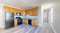 Located at 309 Market St in downtown Harrisburg, Pennsylvania, this one-bedroom, one-bathroom unit offers a practical and well-organized single-floor layout. The kitchen serves as a functional centerpiece, featuring warm honey-toned wood cabinetry extending to the ceiling for generous storage, granite-style countertops, and a full suite of black appliances including a refrigerator, electric range, built-in microwave, and dishwasher. Light wood-look vinyl plank flooring runs throughout the kitchen and living area, lending a clean, contemporary feel. Large multi-pane windows flood the living space with natural light and frame views of the surrounding Harrisburg cityscape. The bedroom is a comfortable size, finished with plush wall-to-wall carpeting and multiple windows fitted with horizontal blinds for adjustable light control. The bathroom is clean and straightforward, appointed with a full-size tub and shower combination, a toilet, and wood-tone tile flooring. A hallway connects the rooms, maintaining a logical and efficient flow throughout the unit. The neutral gray and beige color palette throughout creates a calm, move-in-ready environment suited for urban living.