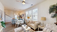 Located at 388 Hinson Dr in Myrtle Beach, SC, this two-story home blends coastal charm with modern comfort throughout its well-designed layout. The open-concept main level features a bright living area anchored by a tufted sofa, a ceiling fan, and large windows dressed with white blinds that invite abundant natural light. Hardwood-style flooring flows seamlessly into the dining area, where a round white table and elegant chairs sit adjacent to the kitchen. The kitchen is well-appointed with gray shaker-style cabinetry, white countertops, stainless steel appliances including a refrigerator, range, and microwave, a peninsula with bar seating, and pendant lighting. A door from the kitchen provides direct access to the fenced outdoor area. The entryway makes a welcoming impression with neutral tones and coastal-inspired décor. Upstairs, bedrooms are comfortably sized with ceiling fans, hardwood-style flooring, and access to an outdoor balcony in at least one room. A clean, bright bathroom with a white vanity and natural window light serves the upper level. A dedicated laundry room with wire shelving, washer hookup, and a water heater adds everyday convenience. Throughout, the home maintains a light, airy coastal aesthetic.
