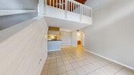 Located at 2350 Cypress Pond Rd in Palm Harbor, Florida, this two-story residence offers a distinctive architectural character defined by its dramatic vaulted wood-plank ceiling, which crowns both the main living area and the upper loft level. The main floor opens into a bright, open-concept layout where the living and dining areas flow seamlessly together, finished with large neutral ceramic tile flooring. The kitchen features a peninsula with a rich wood-toned countertop, ample light wood cabinetry, stainless appliances, and a window that brings in natural light and outdoor views. A white-paneled staircase with a classic balustrade connects the two levels and serves as a visual centerpiece of the space. The upper floor is a versatile loft-style living area bathed in natural light from multiple windows, featuring warm luxury vinyl plank flooring and a ceiling fan beneath the soaring wood ceiling. The bedroom is a calm, light-filled retreat with hardwood-style flooring, a walk-in closet, and a large window overlooking lush Florida greenery. Four bathrooms provide ample convenience, with tile flooring and tub-shower combinations. Multiple closets and storage spaces add practical functionality throughout. The overall ambiance is bright, airy, and warm, with a Florida casual aesthetic.