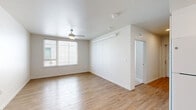 This single-floor, 3-bedroom, 2-bathroom residence offers a clean, modern aesthetic defined by bright white walls, light wood-style flooring, and a neutral color palette throughout. The open living area is highlighted by a ceiling fan with light fixture and a large window fitted with horizontal blinds, allowing natural light to fill the space with a warm, airy ambiance. A stylish sliding barn door adds a contemporary architectural touch, connecting the living area to the rest of the unit. The kitchen is efficiently designed with white shaker-style cabinetry, light stone countertops, white appliances including a refrigerator, electric range, and dishwasher, complemented by recessed lighting and wood-style flooring that extends from the main living area. The two bathrooms feature white vanities with stone countertops, large mirrors, and matching light wood flooring. Each of the three bedrooms is carpeted for comfort, equipped with ceiling fans, and features windows that bring in natural light. Two bedrooms include dedicated closets with sliding panel doors, providing practical storage solutions. The layout flows intuitively, making efficient use of its footprint while maintaining a cohesive, well-lit, and move-in ready feel throughout.