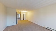 Located at 604 Devils Foot Rd in North Kingstown, Rhode Island, this two-bedroom, one-bathroom residence offers a practical and well-organized single-floor layout. The living area is generously proportioned, featuring neutral-toned wall-to-wall carpeting, clean white walls, and a classic chandelier that adds a touch of warmth. A baseboard heating system runs along the walls, ensuring year-round comfort. A bi-fold closet door provides convenient storage access directly from the living space.

The spacious primary bedroom is a standout feature, offering ample room for furnishings, with two windows that invite natural light and frame views of the surrounding wooded landscape. A wall-mounted air conditioning unit provides additional climate control. The second bedroom is equally well-lit, with carpeted floors and easy access to the rest of the unit.

The galley-style kitchen is efficiently designed, featuring warm wood cabinetry, white countertops, a coil electric range, a dishwasher, and light ceramic tile flooring. The bathroom is bright and clean, with white tile flooring, a natural light window overlooking greenery, and a baseboard heater. Overall, the space presents a functional and comfortable living environment with a quiet, nature-adjacent setting.