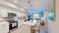 Mayla Apartments Unit 215 is a thoughtfully designed 2-bedroom, 2-bathroom residence located in Pompano Beach, Florida. The open-concept living area seamlessly connects the kitchen, dining, and living spaces, creating a bright and airy atmosphere. The kitchen is outfitted with sleek white cabinetry, a gray tile backsplash, stainless steel appliances, and a spacious white quartz island with bar seating, illuminated by elegant pendant lighting. Wood-look flooring flows throughout the main living areas, adding warmth and continuity. The living room opens to a private balcony through sliding glass doors, offering views of lush tropical landscaping. Soft blue accent walls and neutral tones give the space a calm, coastal character. Each bedroom is generously sized, featuring plush carpeting, large windows with natural light, and a soothing color palette. The primary bathroom features large-format beige tile surrounding a soaking tub, while the second bathroom offers a tub-shower combination with wood-look tile flooring. Recessed lighting throughout ensures a clean, modern finish. This residence combines contemporary design with comfort, making it an inviting home in the heart of South Florida.