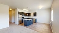 Located at 2300 Main St in Washougal, WA, this well-appointed single-floor residence offers two bedrooms and two full bathrooms across a thoughtfully designed layout. The open-concept kitchen and living area serves as the heart of the home, featuring rich dark cabinetry, light quartz countertops, a center island with bar seating, stainless steel appliances including a refrigerator, range, microwave, and dishwasher, and warm wood-look flooring illuminated by pendant lighting. The spacious living room flows seamlessly from the kitchen and opens to a private balcony through a sliding glass door, offering pleasant outdoor views. Bedrooms are carpeted for comfort; the primary bedroom is generously sized and includes a ceiling fan, a window with natural light, and access to a walk-in closet outfitted with wire shelving. The two bathrooms are clean and functional — one features a shower-tub combination, while the other includes a standalone walk-in shower, both with dark wood vanities and light countertops. Two hallways connect the rooms efficiently throughout the residence. The overall aesthetic is modern and neutral, with white walls, plush carpet in the bedrooms, and durable flooring in the main living areas, creating a clean and versatile living environment.
