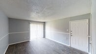 This single-story unit at 2900 S Collins St in Arlington, Texas, presents a practical and updated layout across several well-defined living spaces. The main living area features wood-style plank flooring and neutral gray walls divided by a mid-height chair rail, lending a clean, structured appearance. Vertical blinds cover a sliding glass door that introduces natural light and provides access to the exterior. A textured ceiling runs throughout the main living space, adding subtle visual interest.

The kitchen is notably updated, showcasing white cabinetry, granite-style countertops, and a gray subway tile backsplash. A stainless steel double-basin sink with a contemporary faucet anchors the workspace, complemented by black appliances including an electric range and dishwasher, plus an over-the-range microwave.

The bedrooms are carpeted in a warm neutral tone, each featuring a ceiling fan with integrated lighting and a window fitted with horizontal blinds, allowing for natural light while maintaining privacy. The gray walls carry through cohesively from room to room.

The bathroom is clean and functional, offering a full tub and shower combination with tiled surround, a toilet, and a vanity with a granite-style countertop, framed mirror, and multi-bulb lighting fixture above.