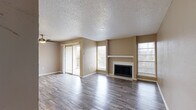 Located in Arlington, TX, this one-bedroom, one-bathroom apartment offers a practical and comfortable single-floor layout. The open living room is a standout, featuring rich wood-look flooring, a ceiling fan, and a tiled fireplace with a white mantle that serves as a natural focal point. Multiple windows fill the space with natural light, and sliding glass doors lead to a private balcony, extending the living area outdoors. The galley-style kitchen is efficiently designed with cream cabinetry, a subway tile backsplash, light stone countertops, and stainless steel appliances including a range and refrigerator. The textured ceilings carry throughout the unit, lending a consistent character to each room. The bedroom is a comfortable size, complete with a ceiling fan, a large sliding-door closet, and a window that allows in natural light. Wood-look flooring continues here, complementing the warm, neutral tones found throughout. The bathroom features a vanity with matching cabinetry and wood-look tile flooring. Throughout the unit, warm beige walls and consistent flooring create a cohesive, move-in-ready aesthetic well-suited for everyday living.