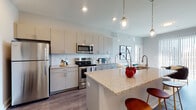 Located at 2875 Olentangy River Rd in Columbus, Ohio, this contemporary single-floor residence offers a well-designed open-concept layout that seamlessly connects the kitchen and living areas. The kitchen is a standout feature, equipped with stainless steel appliances, a subway tile backsplash, light gray cabinetry extending to the ceiling, and a granite-topped island with a double sink and pendant lighting overhead. Wood-style flooring runs throughout the main living areas, adding warmth and continuity to the space. The living room is bathed in natural light through floor-to-ceiling sliding glass doors that open to an outdoor balcony, offering views of the surrounding Columbus area. The bedrooms are carpeted and well-lit by large windows with horizontal blinds, providing a comfortable and restful atmosphere. Each bedroom is generously sized with ample closet space. The bathrooms are thoughtfully appointed with granite vanity countertops, gray cabinetry, framed mirrors, and modern light fixtures. One bathroom features a tub-shower combination with elegant marble-style tile surround. A walk-in closet with wire shelving connects directly to one of the bathrooms, enhancing everyday functionality. The overall palette of soft grays and whites gives the space a clean, modern, and inviting ambiance throughout.