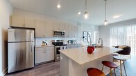 Located at 2875 Olentangy River Rd in Columbus, Ohio, this contemporary single-floor residence offers a well-designed open-concept layout that seamlessly connects the kitchen and living areas. The kitchen is a standout feature, equipped with stainless steel appliances, a subway tile backsplash, light gray cabinetry extending to the ceiling, and a granite-topped island with a double sink and pendant lighting overhead. Wood-style flooring runs throughout the main living areas, adding warmth and continuity to the space. The living room is bathed in natural light through floor-to-ceiling sliding glass doors that open to an outdoor balcony, offering views of the surrounding Columbus area. The bedrooms are carpeted and well-lit by large windows with horizontal blinds, providing a comfortable and restful atmosphere. Each bedroom is generously sized with ample closet space. The bathrooms are thoughtfully appointed with granite vanity countertops, gray cabinetry, framed mirrors, and modern light fixtures. One bathroom features a tub-shower combination with elegant marble-style tile surround. A walk-in closet with wire shelving connects directly to one of the bathrooms, enhancing everyday functionality. The overall palette of soft grays and whites gives the space a clean, modern, and inviting ambiance throughout.