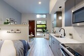 Located at 222 Mercer St in Seattle's South Lake Union neighborhood, this efficiently designed studio offers a thoughtful open-concept layout that maximizes every square foot. Light wood-look flooring runs throughout, lending warmth and visual continuity across all areas.

The combined dining, kitchen, and living area forms the heart of the unit. The kitchen features sleek grey cabinetry, a white quartz countertop, subway tile backsplash, stainless steel appliances, an undermount sink with a matte black faucet, and stylish pendant lighting. A low half-wall partition subtly defines the sleeping area without closing off the open feel of the space.

The entrance area benefits from an oversized floor-to-ceiling window and transom window above, flooding the interior with natural light and offering direct views onto the private patio. A barn-style sliding door adds a modern architectural accent. The patio extends the living space outdoors, ideal for enjoying Seattle's scenic surroundings.

The bathroom and laundry room is clean and contemporary, finished with the same light wood-look flooring, a dark vanity with a white countertop, large mirror, and updated fixtures. A dedicated closet provides practical storage. Recessed lighting throughout the unit completes the polished, modern aesthetic.