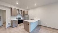 Located at 1305 Harris Avenue in Bellingham, WA, this well-designed 2-bedroom, 1-bathroom unit offers a thoughtful layout across a single floor. The modern kitchen serves as a central highlight, featuring taupe shaker-style cabinetry, crisp white countertops, a peninsula island with an undermount sink, and a full suite of stainless steel appliances including a range with a wall-mounted ventilation hood and a full-size refrigerator. Light wood-style luxury vinyl flooring runs consistently throughout the unit, lending a clean, cohesive aesthetic. The primary bedroom is generously sized and includes a large sliding window with a balcony access, offering pleasant views of surrounding greenery. The second bedroom features a built-in closet with sliding doors, providing practical storage. A dedicated closet space and a hallway connect the rooms efficiently. The full bathroom is outfitted with a white soaking tub and shower combination with chrome fixtures. Neutral wall tones and recessed lighting throughout contribute to a bright, contemporary ambiance. The unit's efficient and functional design makes it a well-appointed space in the heart of Bellingham.