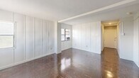 Located at 1230 Pendleton Street in Columbia, SC, Unit 11H is a one-bedroom, one-bathroom residence spread across a single floor. The layout is efficiently organized, with multiple hallways connecting the main living areas and providing a sense of flow throughout the unit.

The living area is a standout feature, offering a spacious open feel with tall white panel-detailed walls, a large white ceiling, and rich, glossy dark parquet flooring that adds warmth and character. Natural light enters through multiple windows, each equipped with a window-mounted air conditioning unit. The clean white walls and wide floor plan give the room a bright, airy atmosphere.

The kitchen is well-appointed with white cabinetry — both upper and lower — complemented by a bold dark marbled countertop that provides a striking visual contrast. Open shelving, a coil electric range, and a sink round out the functional workspace.

The bedroom is a cozy, private space with the same rich parquet flooring and a window that brings in natural light. The bathroom features a full tub-shower combination with white tile surround, a classic chrome showerhead, and a pedestal sink, maintaining a clean and timeless aesthetic throughout.

Overall, the unit presents a straightforward and functional layout with classic design elements, making it a practical and comfortable living space.