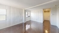 Located at 1230 Pendleton Street in Columbia, SC, Unit 11H is a one-bedroom, one-bathroom residence spread across a single floor. The layout is efficiently organized, with multiple hallways connecting the main living areas and providing a sense of flow throughout the unit.

The living area is a standout feature, offering a spacious open feel with tall white panel-detailed walls, a large white ceiling, and rich, glossy dark parquet flooring that adds warmth and character. Natural light enters through multiple windows, each equipped with a window-mounted air conditioning unit. The clean white walls and wide floor plan give the room a bright, airy atmosphere.

The kitchen is well-appointed with white cabinetry — both upper and lower — complemented by a bold dark marbled countertop that provides a striking visual contrast. Open shelving, a coil electric range, and a sink round out the functional workspace.

The bedroom is a cozy, private space with the same rich parquet flooring and a window that brings in natural light. The bathroom features a full tub-shower combination with white tile surround, a classic chrome showerhead, and a pedestal sink, maintaining a clean and timeless aesthetic throughout.

Overall, the unit presents a straightforward and functional layout with classic design elements, making it a practical and comfortable living space.