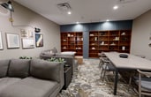 This 370 square foot space in White Plains, NY, showcases a thoughtfully designed interior that maximizes functionality in a compact area. The room is divided into two main sections: a cozy living area and a versatile workspace. The living area features a comfortable gray sectional sofa, complemented by a round marble-top table. A curated gallery wall adds visual interest, displaying a mix of abstract and geometric artworks.

The workspace is defined by a large rectangular table with seating for six, ideal for meetings or collaborative work. A striking feature is the floor-to-ceiling built-in shelving unit, painted in a deep blue that contrasts beautifully with the warm wood interior. This storage solution not only provides ample space for books and decorative items but also adds a sophisticated touch to the room.

Throughout the space, the flooring consists of a unique marbled pattern, adding texture and visual depth. The walls are painted in a neutral tone, creating a calm backdrop for the furniture and artwork. Lighting is thoughtfully placed, with recessed ceiling lights and adjustable wall-mounted fixtures providing both ambient and task lighting.

The room's design emphasizes a balance between aesthetics and practicality, making efficient use of the limited square footage while maintaining a stylish and inviting atmosphere. This space is well-suited for a variety of purposes, from a small office to a multi-functional living area in a compact urban setting.