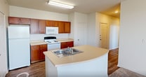 This single-floor apartment at 1800 Post Road, Unit 1432 in San Marcos, Texas offers a practical and comfortable layout designed for everyday living. The kitchen is a functional centerpiece of the unit, featuring warm wood-toned cabinetry, light countertops, a curved island with a built-in sink, and white appliances including a refrigerator, electric range, and microwave. Wood-look flooring runs through the kitchen and main living areas, adding a clean, cohesive aesthetic. The living space includes a dedicated entry area with built-in wall shelving and a glass-panel door that allows natural light to filter in. Multiple bedrooms are carpeted for comfort and each includes a ceiling fan with light fixture and windows with horizontal blinds that provide views of the surrounding greenery. Closet access is available in the bedrooms via classic six-panel white doors. The bathrooms are finished with white subway-style tile surrounding the tub-shower combinations, wood-toned cabinetry for storage, and wood-look flooring. Natural light is present throughout the unit via multiple windows. The overall design is neutral and clean, offering a move-in ready environment with a straightforward, well-organized floor plan.
