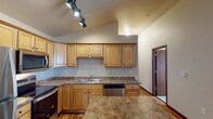 This single-floor unit offers a thoughtfully designed layout that balances functionality and comfort. The kitchen serves as a central highlight, featuring warm honey-toned wood cabinetry, granite-style countertops, and a full suite of stainless steel appliances including a refrigerator, electric range, over-the-range microwave, and dishwasher. A kitchen island provides additional prep and seating space, and track lighting illuminates the area beneath vaulted ceilings that lend an open, airy feel. The kitchen flows seamlessly into the open-concept living area, which is anchored by a ceiling fan and access to an outdoor balcony, allowing for natural light and ventilation. Durable wood-look flooring runs throughout the main living areas, while plush carpeting adds warmth to the bedrooms. The primary bedroom features vaulted ceilings, a ceiling fan, a window for natural light, and direct access to a private bathroom equipped with a shower-tub combo. A second bedroom with soft carpet and neutral walls provides a comfortable and versatile space. A half bathroom with a vanity and mirror serves as a convenient powder room. Rich wood door trim and baseboard accents tie the interior together with a cohesive, classic aesthetic throughout the unit.