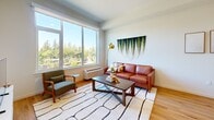 Located in Tigard, Oregon, this thoughtfully designed one-bedroom, two-bathroom residence offers a comfortable and contemporary living experience across a single floor. The open-concept layout seamlessly connects the kitchen and living room, creating a cohesive and functional space ideal for both daily living and entertaining.

The kitchen is a standout feature, boasting warm wood-toned cabinetry, a striking blue tile backsplash, stainless steel appliances, and a spacious island with a white quartz countertop and bar seating beneath sleek pendant lighting. Hardwood-style flooring flows consistently throughout the unit, contributing to a warm and cohesive aesthetic.

The living room is bathed in natural light through large picture windows that frame views of lush, mature trees, creating a serene and airy atmosphere. The bedroom is a well-proportioned retreat, filled with natural light from its own window with greenery views, and features direct access to a generously sized walk-in closet with built-in shelving and hanging storage. The two bathrooms are clean and modern, with one featuring a full soaking tub and shower combination. Crisp white walls and warm wood flooring throughout tie the space together with a cohesive, contemporary feel.