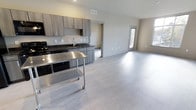 This Type C residence features 2 bedrooms and 2 bathrooms across a single thoughtfully arranged floor. The open-concept layout seamlessly connects the kitchen and living areas, creating a bright and functional space that feels expansive and welcoming. The kitchen is outfitted with contemporary gray cabinetry, dark granite countertops, and a stainless steel sink, complemented by black appliances. A movable stainless steel utility cart adds a versatile, modern touch to the culinary space. Light-toned luxury vinyl plank flooring extends throughout the main living area, lending a clean, cohesive aesthetic that reflects natural light beautifully. The living area is generously proportioned, with neutral wall tones and multiple windows that invite natural light and provide views to the outdoors. Recessed ceiling vents ensure efficient climate control throughout. Doorways lead to the private bedroom and bathroom quarters, maintaining a clear separation between living and sleeping spaces. The overall ambiance is modern and move-in ready, with a neutral palette that offers flexibility for personalization. This residence is an ideal choice for those seeking a practical yet stylish home with a well-balanced floor plan.
