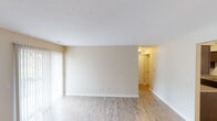 This single-floor residence offers a practical and comfortable layout designed for easy living. The open living and dining area is finished with light wood-style flooring that extends throughout the main living spaces, creating a bright and cohesive feel. Neutral beige walls and white trim provide a clean, versatile backdrop, while vertical blinds along the sliding glass door allow for natural light control. The kitchen is thoughtfully equipped with dark espresso cabinetry, granite-style countertops, a stainless steel sink, and black appliances including a refrigerator and range. The galley-style layout maximizes storage and counter space efficiently. A hallway connects the living area to the private quarters, where the bedrooms feature soft wall-to-wall carpeting and windows dressed with horizontal blinds that bring in natural light and offer outdoor views. The textured ceilings add a subtle dimensional detail throughout the space. A bathroom with tile flooring and towel bars is conveniently accessible from the hallway. Overall, the space presents a functional, move-in-ready environment with a consistent neutral palette and durable finishes suited for everyday living.