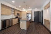 Located at 1800 E Gene Autry Way in Anaheim, California, this single-floor residence offers a thoughtfully designed layout with a clean, contemporary aesthetic. The open-concept living area features warm wood-look flooring, recessed lighting, and a ceiling fan, flowing seamlessly into the kitchen and dining space.

The kitchen is well-equipped with light wood cabinetry extending to the ceiling for ample storage, stainless steel appliances including a gas range, microwave, refrigerator with ice maker, and dishwasher, along with a wine cooler. A central island with a dark countertop provides additional workspace and serves as a natural gathering point. Pendant lighting accents the space alongside recessed fixtures.

The bedrooms offer plush carpeting, ceiling fans, and windows with blinds that invite natural light. Each room provides a comfortable, versatile space with walk-in or reach-in closet options visible in select rooms. The bathrooms feature light wood vanities with dark countertops, modern fixtures, and a combination tub and shower. The primary bath includes a dual-sink vanity and stylish barn-style doors, while a secondary bath offers a tall window for added brightness.
