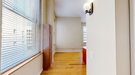 Located at 142 Fifth St E in downtown Saint Paul, this two-bedroom, two-bathroom residence offers a well-organized single-floor layout with a cohesive, neutral design palette throughout. The open-concept kitchen and living area serves as the heart of the home, anchored by a central island with a granite countertop, double sink, and warm cherry wood cabinetry. Stainless steel appliances, including a refrigerator, range, and microwave, add a modern touch, while soaring ceilings and a ceiling fan lend the living space an airy, expansive feel. Large windows with blinds invite abundant natural light and frame urban views of the surrounding Saint Paul cityscape. The flooring transitions between classic hardwood and stone tile, adding textural variety across the living and kitchen zones. Both bedrooms are comfortably sized, each featuring hardwood floors and windows with city views. The primary bedroom benefits from its own en-suite bathroom equipped with a glass-enclosed shower and vanity. A second full bathroom includes a bathtub and a stacked washer-dryer unit for added convenience. A hallway connects the rooms efficiently, completing this practical and well-appointed urban residence.