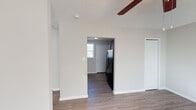 This single-story unit offers a practical and well-organized layout throughout. The kitchen is equipped with rich dark espresso cabinetry providing ample upper and lower storage, dark speckled countertops, and a stainless steel double-basin sink. A window fitted with horizontal blinds allows natural light to filter into the space, while a range hood and stove are also present. A door from the kitchen provides direct exterior access.

The living areas feature wood-look laminate flooring in a light tone, neutral warm-beige walls, and textured ceilings. Ceiling fans are present in multiple rooms, contributing to air circulation and comfort. Several rooms benefit from multiple windows dressed with horizontal blinds, filling the spaces with generous natural light. One room includes a wall-mounted HVAC unit positioned beneath a window. An open passageway connects the living area to the kitchen, where a black refrigerator is visible near the entry door.

The bathroom includes a full tub and shower combination with a curtain rod, a toilet, and wood-look flooring. Throughout the unit, clean white trim, baseboards, and interior doors maintain a cohesive and tidy aesthetic.
