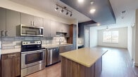 Located at 290 M.L.K. Jr Dr SE in Atlanta, Georgia, this single-floor unit offers a well-designed layout with modern finishes throughout. The kitchen serves as a central highlight, showcasing two-tone cabinetry in taupe and warm wood tones, a full suite of stainless steel appliances including a range, microwave, dishwasher, and refrigerator, and a subway tile backsplash. A center island with a light quartz countertop provides additional prep and dining space, while track lighting and recessed fixtures ensure ample illumination. A built-in desk nook adjacent to the kitchen adds a practical workspace. The open layout connects the kitchen seamlessly to the living area, which features hardwood-style flooring and a ceiling fan. Bedrooms feature soft carpeting and large windows fitted with horizontal blinds, with select rooms offering views of the Atlanta skyline and surrounding greenery. The bathroom is finished with large-format tile flooring, a soaking tub with subway tile surround, a wood-toned vanity, and direct access to a dedicated walk-in closet equipped with shelving. The overall aesthetic is clean, contemporary, and functional.