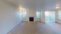 This single-floor unit offers a well-organized layout with distinct living, sleeping, and functional zones. The living room serves as the focal point of the space, featuring a tiled fireplace framed by a white mantel and flanked by two windows dressed with vertical blinds, allowing generous natural light to fill the carpeted room. A sliding door provides additional access and light to the area.

The galley-style kitchen is efficiently designed with light wood cabinetry, dark countertops, tile flooring, and recessed lighting overhead. White appliances — including a refrigerator, electric range, and over-the-range microwave — are neatly integrated into the layout, along with a stainless steel sink positioned beneath a window.

The bedroom areas are carpeted and well-lit, with one room featuring a wide window with a built-in ledge and baseboard heating. Closet space is well-accommodated, including a mirrored sliding-door closet that enhances the sense of space. The bathroom includes a vanity with a laminate countertop, a large mirror, and a separate shower enclosure. Throughout, the unit maintains a neutral, light color palette with a clean and functional aesthetic.