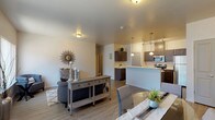 This single-story residence offers a thoughtfully designed open-concept layout that seamlessly connects the living, dining, and kitchen areas. The main living space features wood-look plank flooring, neutral-toned walls, and large windows dressed with vertical blinds that allow generous natural light to fill the room. The open layout provides a spacious, airy feel well-suited for both everyday living and entertaining.

The kitchen is a functional highlight, equipped with dark espresso-toned cabinetry, white countertops, and a full suite of stainless steel appliances including a range, microwave, dishwasher, and refrigerator. Pendant lighting over the kitchen peninsula adds warmth and definition to the space. A dedicated dining area sits adjacent, completing the open living zone.

The bedrooms are carpeted for comfort and each includes a closet with built-in shelving. One bedroom features a sliding window that brings in natural light. The full bathroom offers dark cabinetry with white countertops, a tub-shower combination, and wood-look flooring consistent with the rest of the unit.

A dedicated laundry room houses a full-size washer and dryer with overhead wire shelving for additional storage, adding practical convenience to the overall layout.