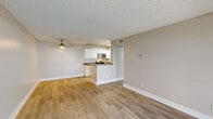 This 1-bedroom, 1-bathroom unit offers a thoughtfully designed single-floor layout with a clean, neutral aesthetic throughout. The open-concept living room and kitchen area forms the heart of the space, featuring light wood-style flooring, warm beige walls, and a textured ceiling. A ceiling fan anchors the living area, adding both function and character. The kitchen is efficiently arranged in a galley style with white cabinetry, dark countertops, and stainless steel appliances including a gas range, microwave, and refrigerator. A peninsula counter separates the kitchen from the living area, providing additional workspace and a natural visual division. A hallway connects the main living area to the private spaces, leading to the generously sized bedroom, which benefits from a sliding glass door that opens onto a private balcony overlooking greenery and landscaping — offering a pleasant outdoor connection and natural light. The bathroom is clean and functional, featuring a tub-shower combination, white vanity cabinetry with dark countertops, a large mirror, and brushed nickel fixtures. Consistent light wood-style flooring flows throughout the entire unit, lending a cohesive and contemporary feel to every room.