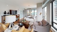 This contemporary urban residence offers a thoughtfully designed open-concept layout that seamlessly connects its living, dining, and kitchen areas. The living room is a standout, bathed in natural light from expansive floor-to-ceiling windows that frame sweeping city views. Exposed ductwork and a striking sputnik chandelier lend the space an industrial-chic character, while warm hardwood flooring flows throughout the main living areas.

The gourmet kitchen is well-appointed with sleek two-tone cabinetry — crisp white uppers paired with dark lower cabinets — complemented by a granite-topped island, a full suite of stainless steel appliances, and a tile backsplash. The kitchen's large windows further enhance the bright, airy atmosphere.

Both bedrooms are carpeted and comfortable, featuring neutral tones and ample room for furnishings. Each is served by its own bathroom, finished with dark vanity cabinetry, white countertops, large-format tile flooring, and clean, modern fixtures. One bathroom includes a walk-in shower, while the other features a shower-tub combination.

A generously sized walk-in closet with wire shelving and a hanging rod provides practical storage. Throughout the residence, the consistent use of neutral grey tones, modern hardware, and quality materials creates a cohesive and polished aesthetic suited to contemporary urban living.