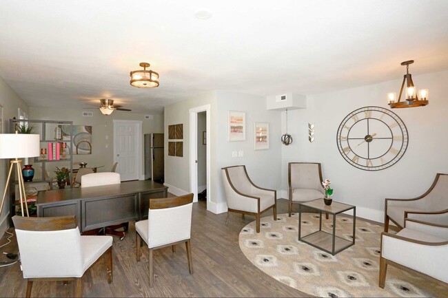 Open-plan living and dining space with hardwood floors, accent chairs, large wall clock, and gold pendant lighting - Bennett Pointe